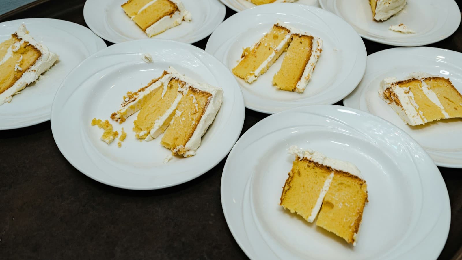 Slices of sponge cake with cream on white plates on a tray