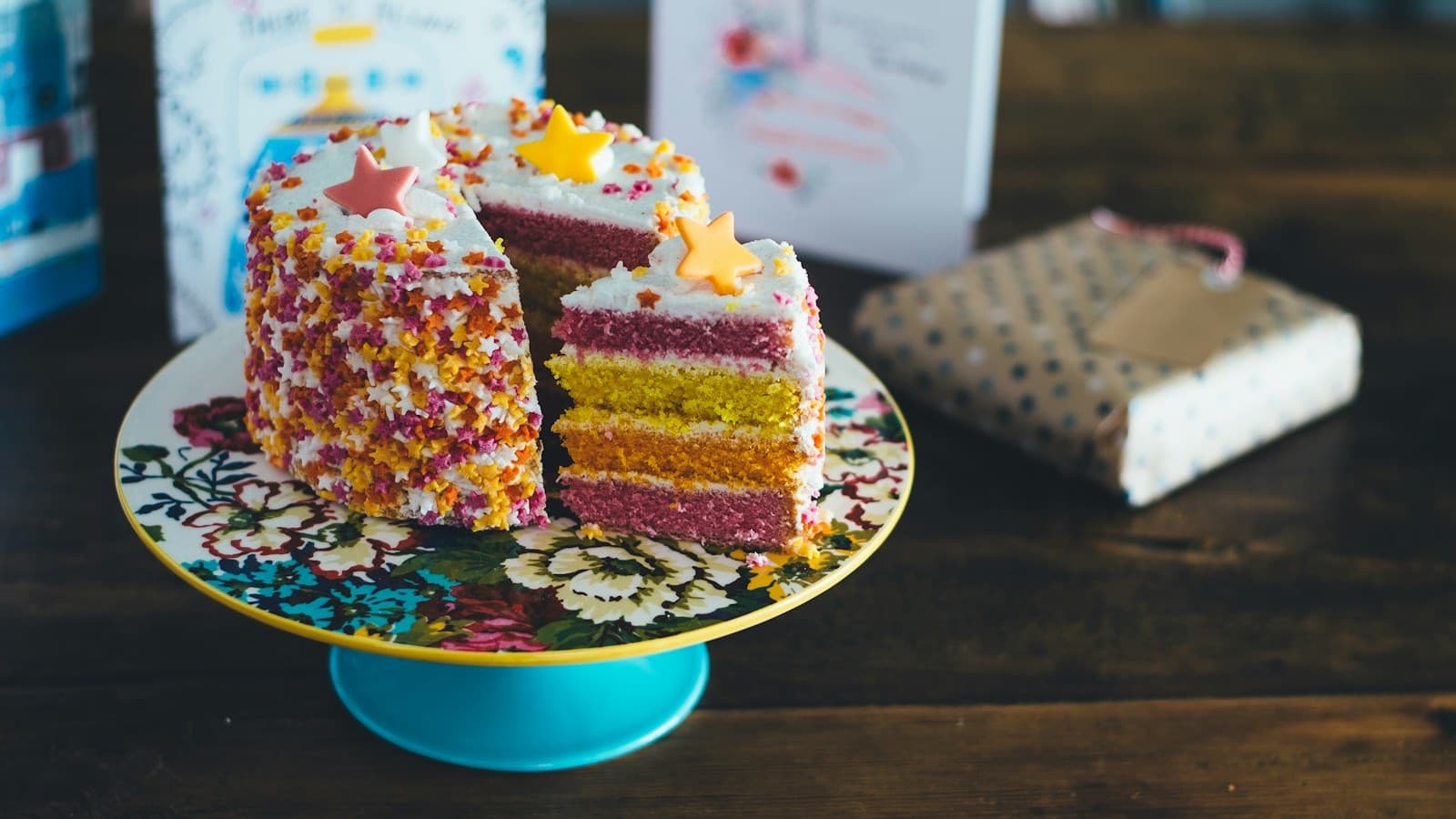 A colorful layer cake with sprinkles and a slice cut out on a cake stand, showing the sponge and cream layers