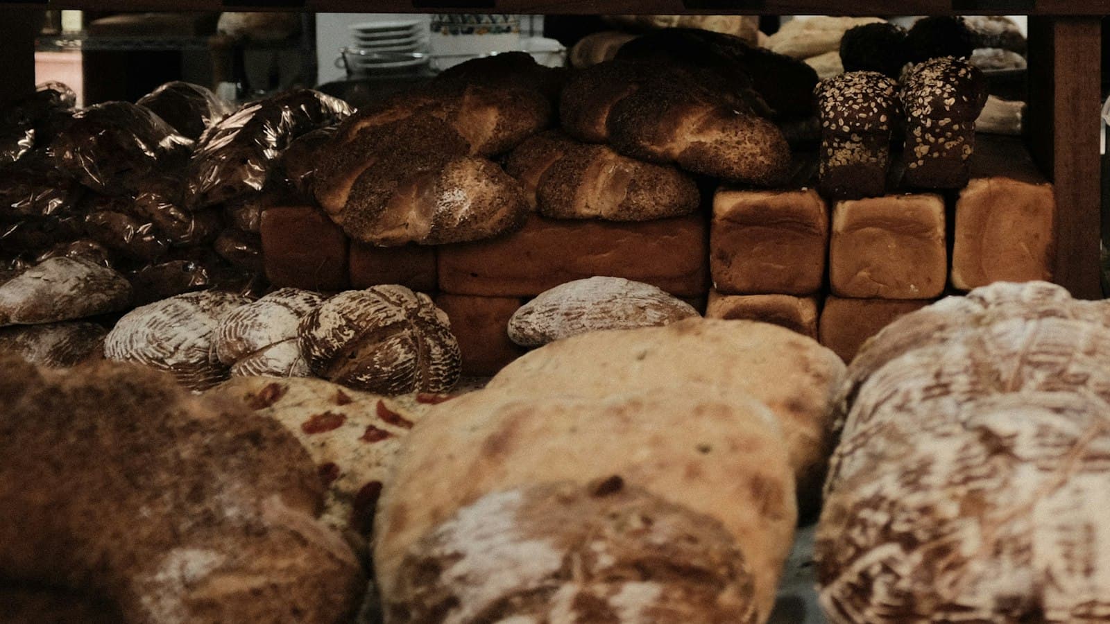 Bakery shelves stacked with sourdough loaves, poppy seed challahs and sandwich loaves in tins