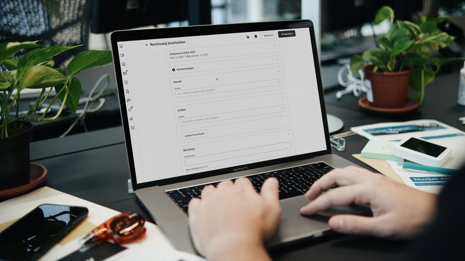 Hands on a laptop keyboard with an invoice form open on the screen, next to documents and a phone
