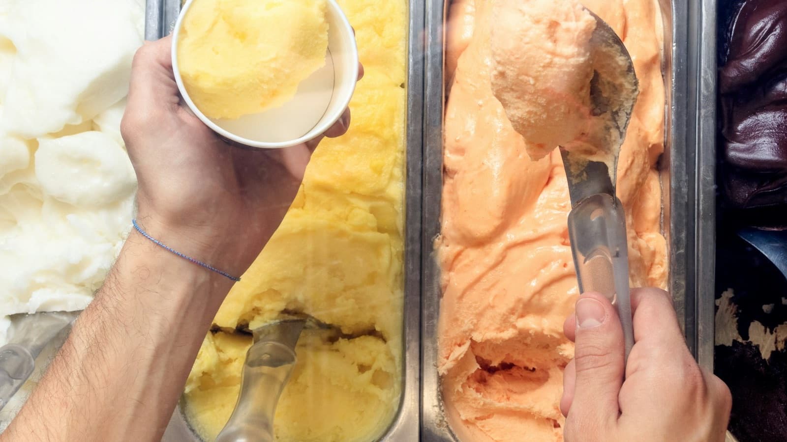 Scooping craft ice cream into a cup from metal pans in an ice cream shop