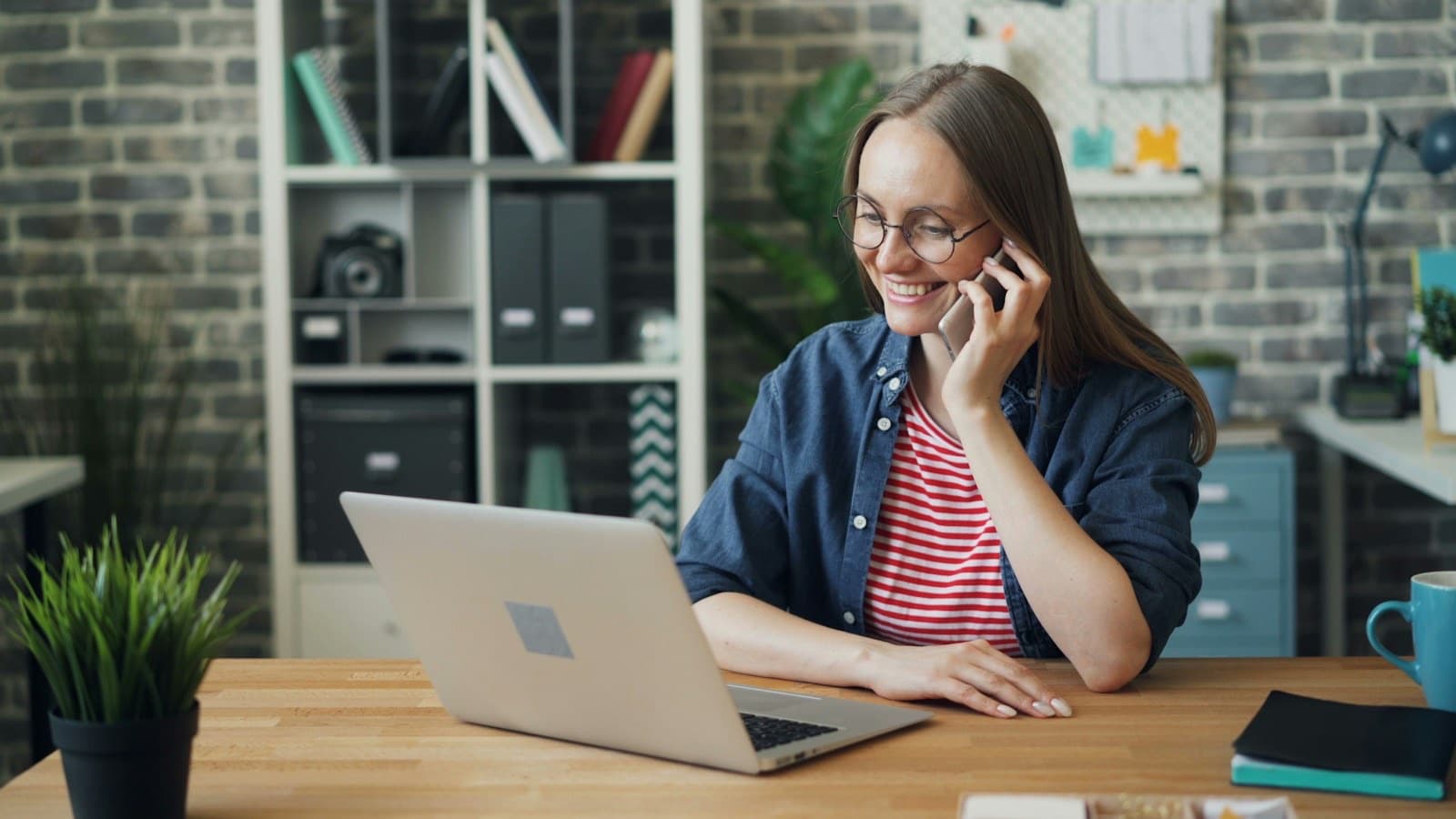 A smiling woman talking on the phone at a desk with a laptop, taking an order