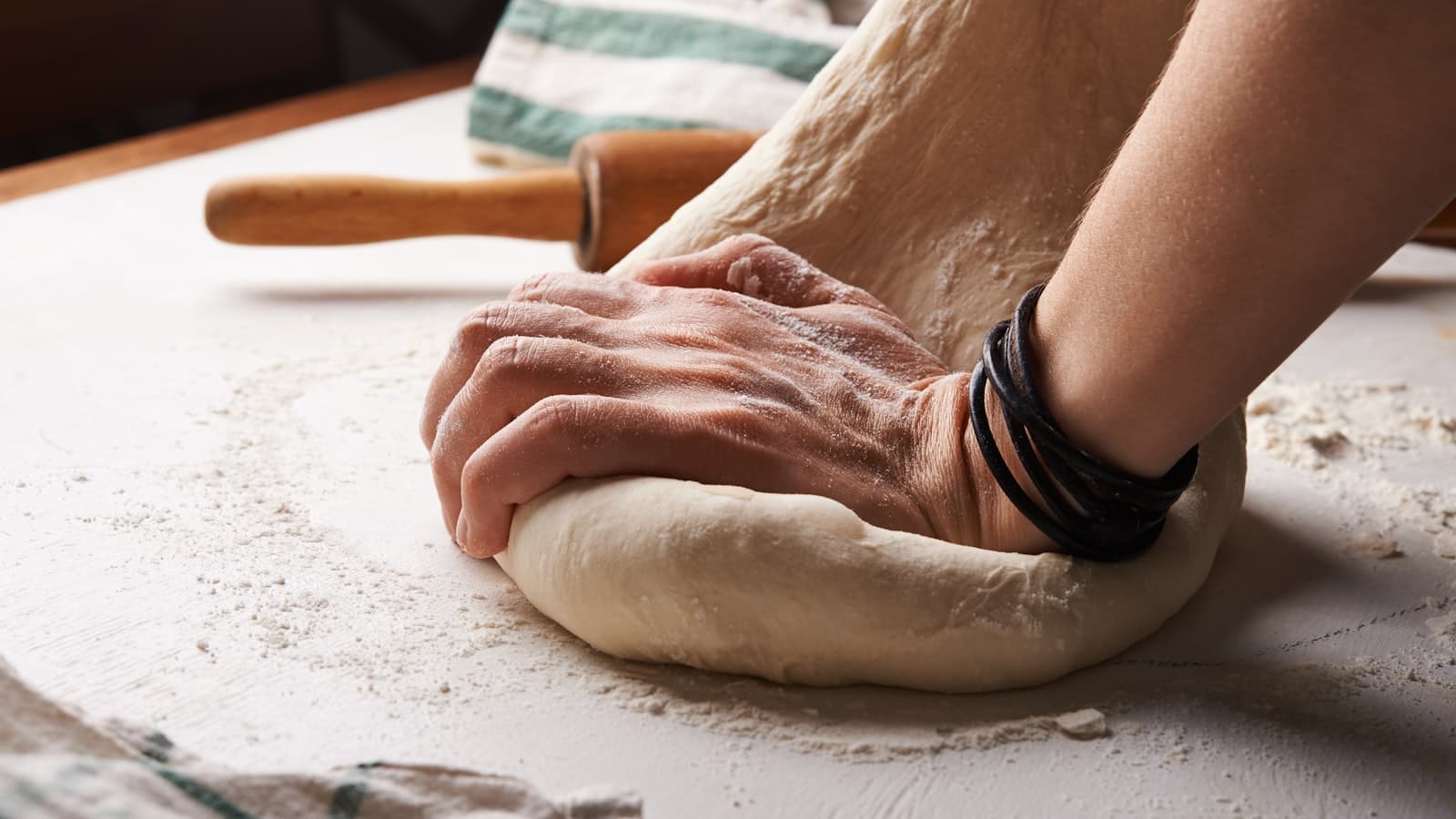 A baker's hands kneading dough on a wooden counter