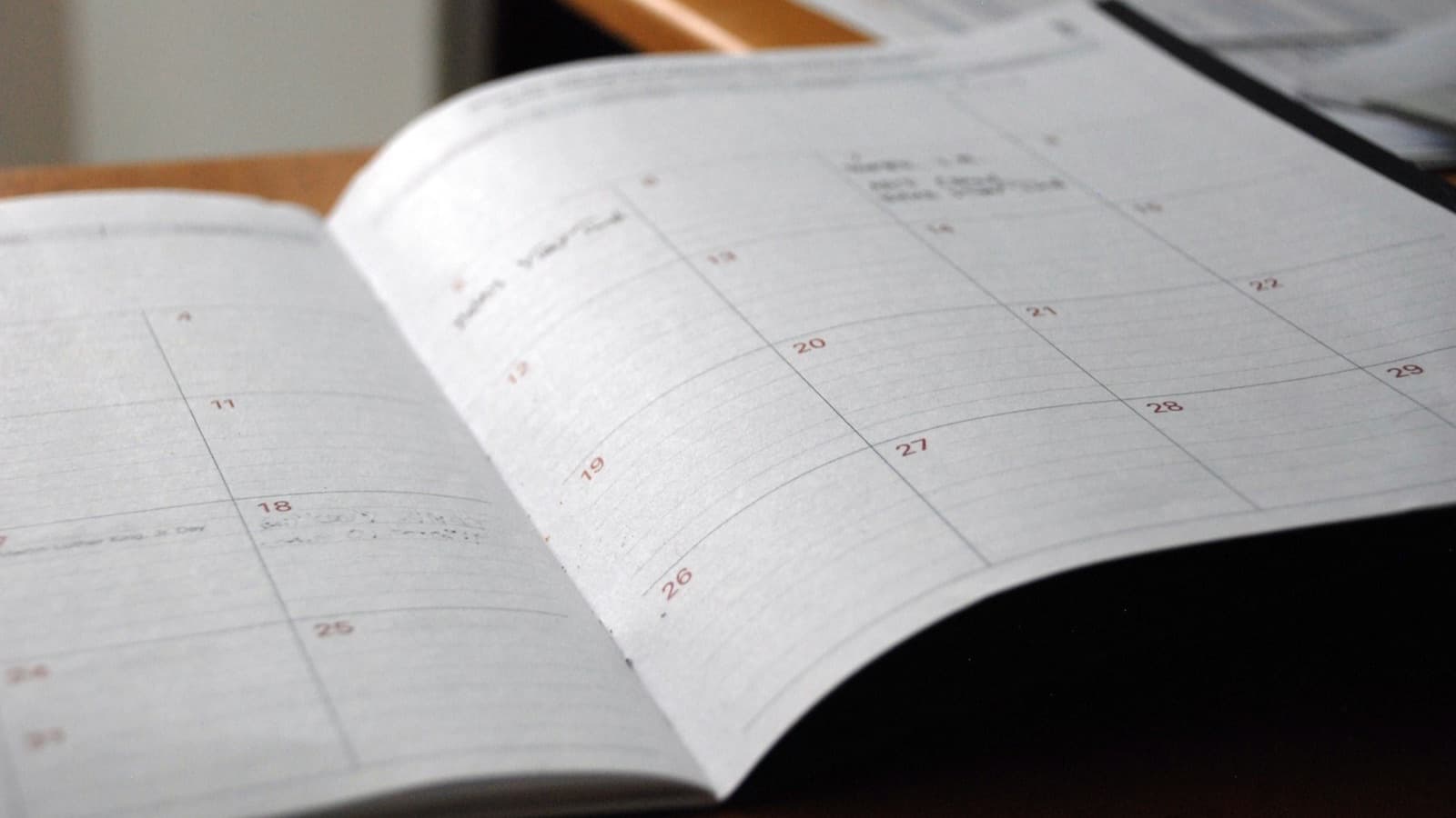 An open monthly planner with a grid of days and handwritten notes on a wooden desk